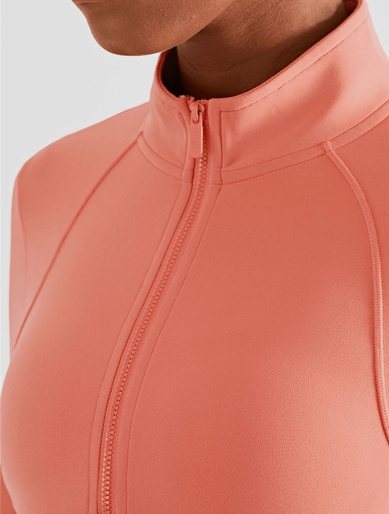 Close-up of peach women's elastic long sleeve fitness sweatshirt with zipper detail and smooth seams, designed for athletes.
